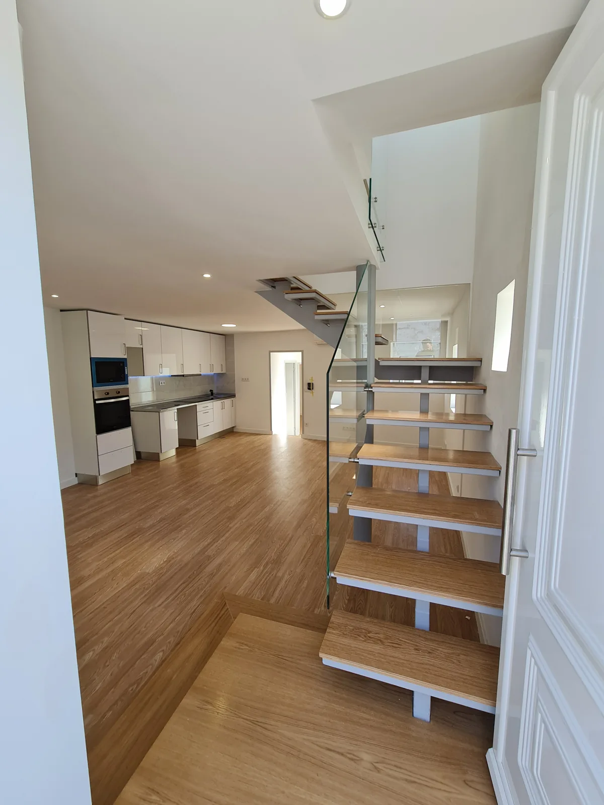 Interior renovado com escada em madeira, guarda em vidro e cozinha integrada