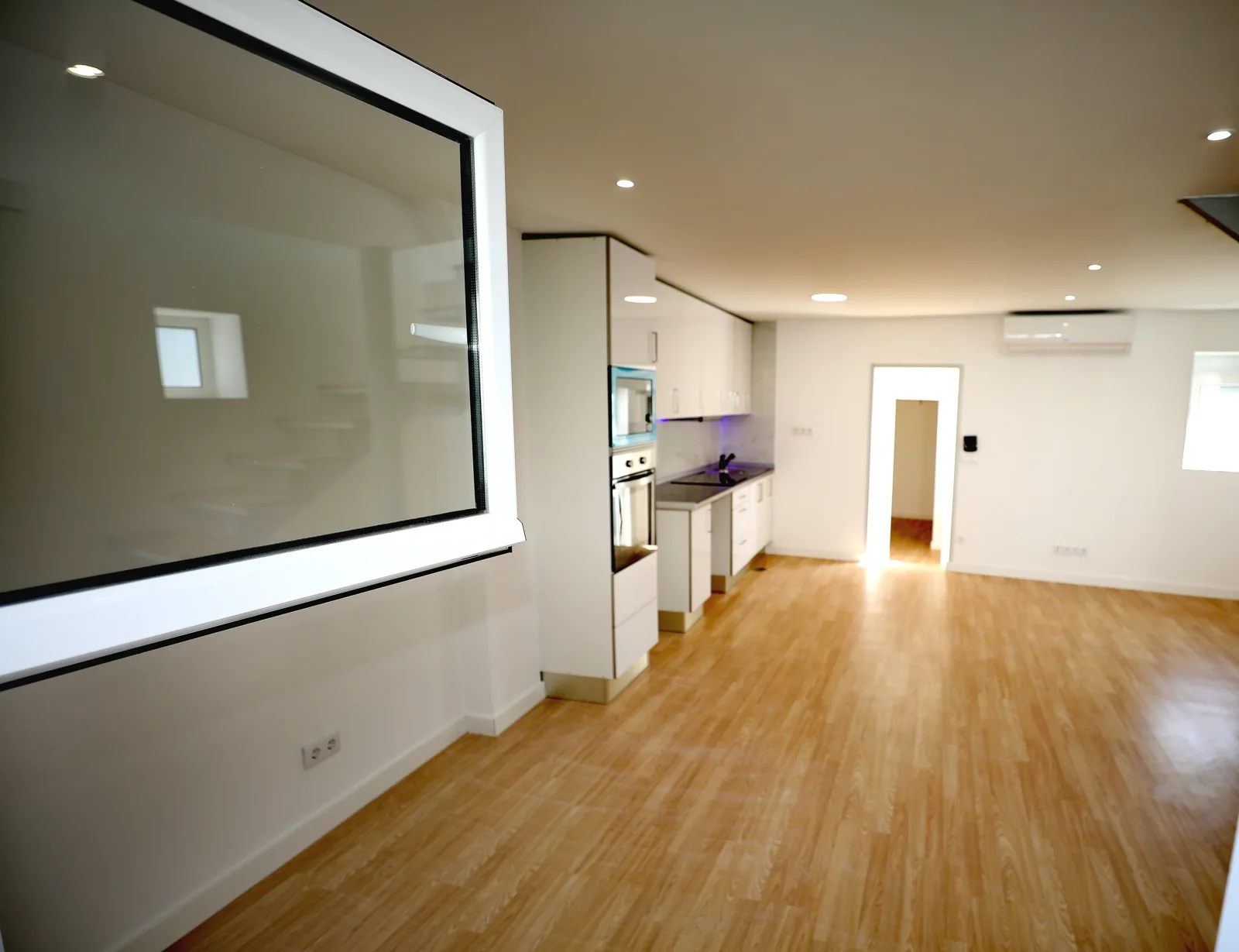 Zona social renovada da Casa Campanhã, com cozinha aberta, pavimento em madeira e iluminação embutida